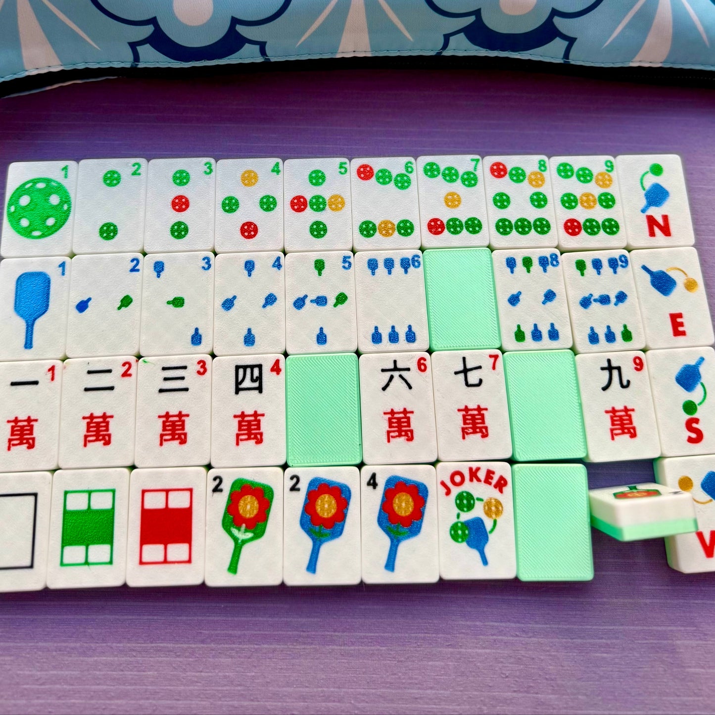 Set of colorful tiles with symbols on a purple surface, next to a blue and white patterned bag.