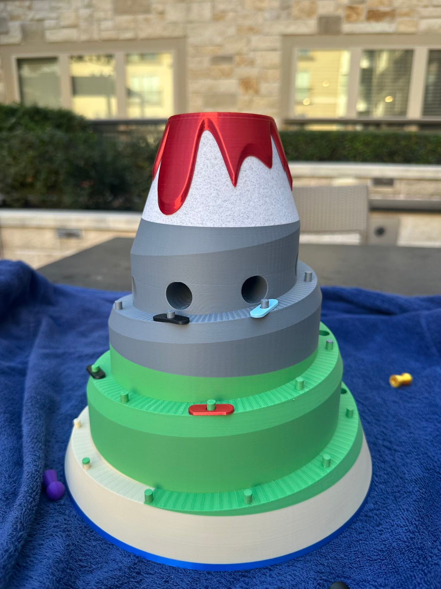 Side view of the Volcano Racer board game with colorful cars climbing the green and gray tiers toward the volcano summit.