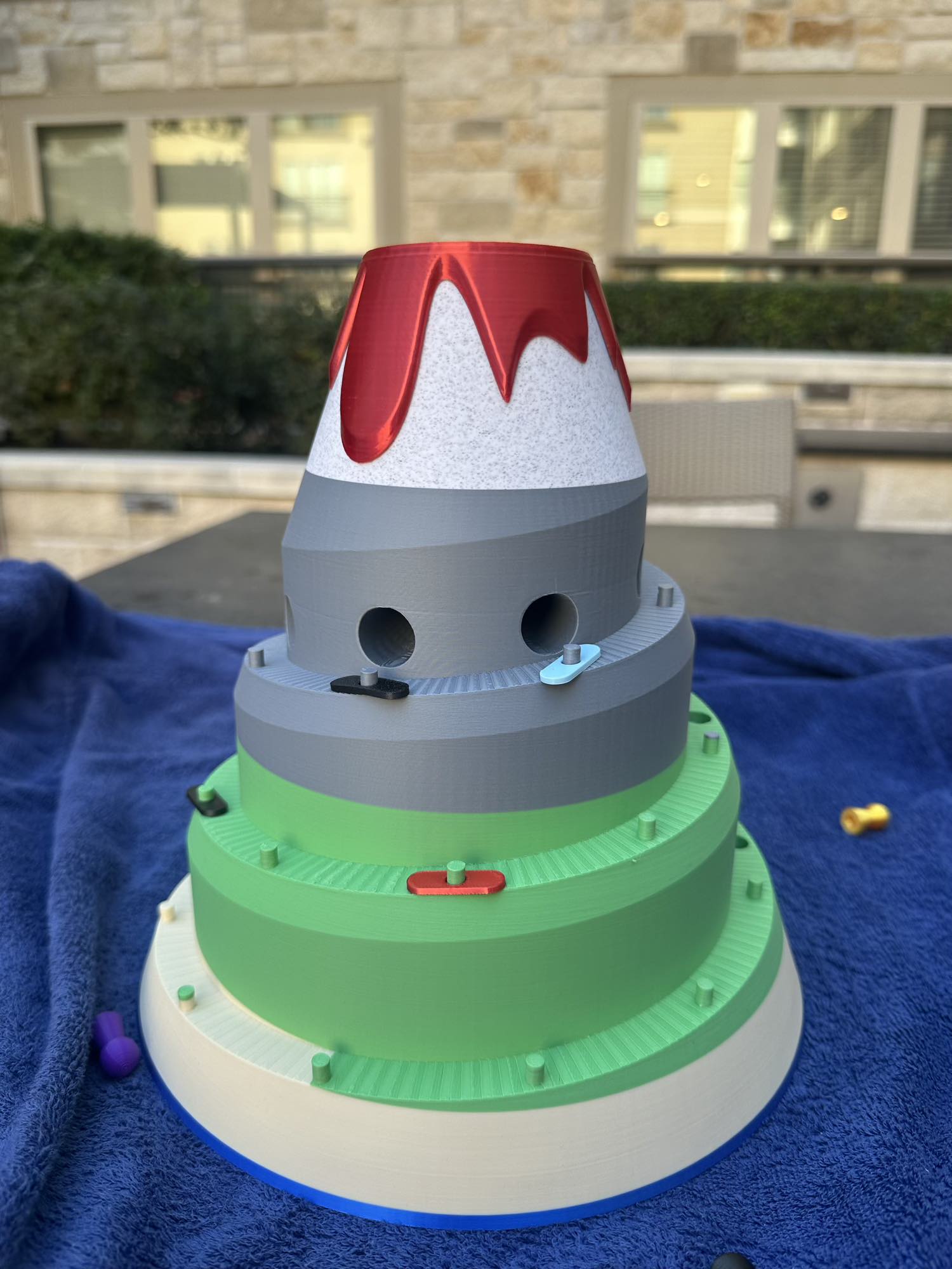 Side view of the Volcano Racer board game with colorful cars climbing the green and gray tiers toward the volcano summit.