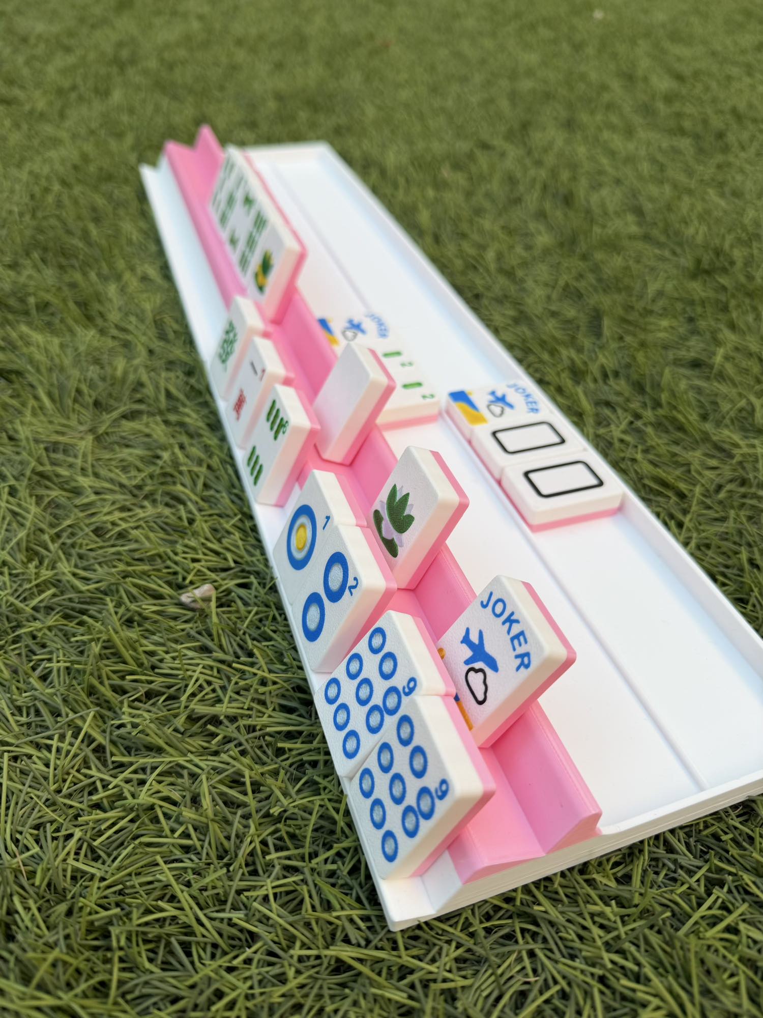 A white Two Player Mahjong rack with pink accents holding a full hand of tiles, including jokers and flowers.