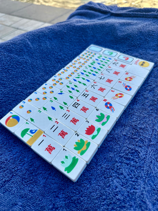 Close-up of floating Mahjong tiles with nautical pool-themed designs, including beach balls, lifebuoys, lotus flowers, and umbrellas, displayed on a towel.