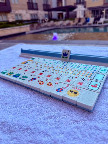 Floating Mahjong tiles in a nautical pool theme with rack, displayed poolside on a towel. Includes colorful beach ball, lifebuoy, lotus, and joker designs.