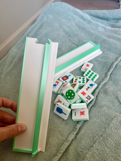 Hand holding a green and white floating mahjong rack beside loose pickleball-themed mahjong tiles on a towel surface.