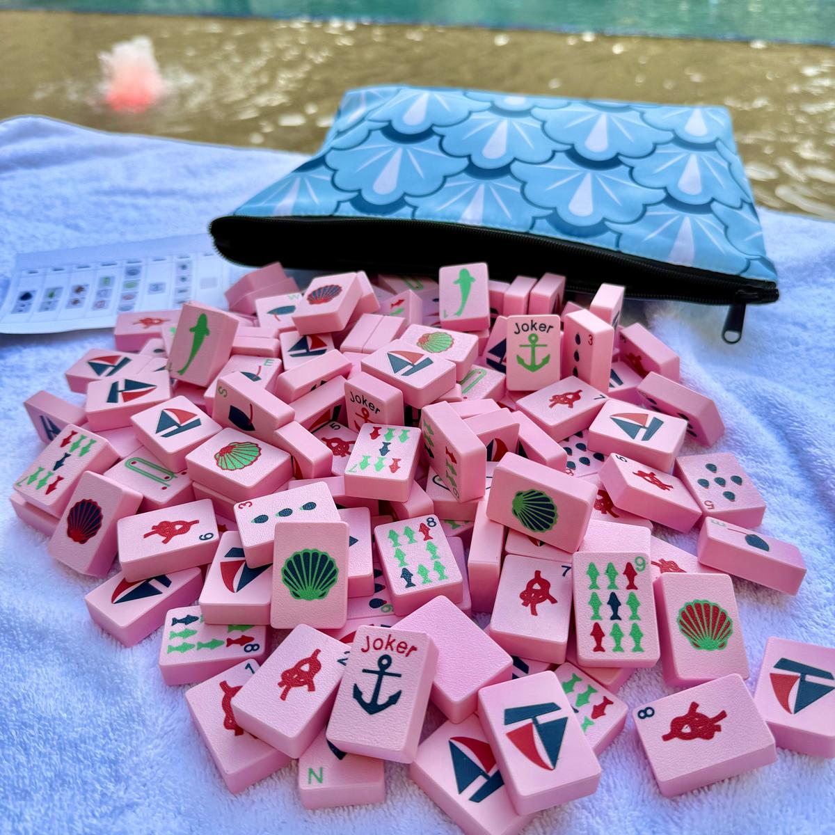 Pink game pieces with symbols on a towel next to a blue pouch by a pool.