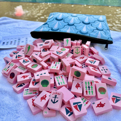 Pink game pieces with symbols on a towel next to a blue pouch by a pool.