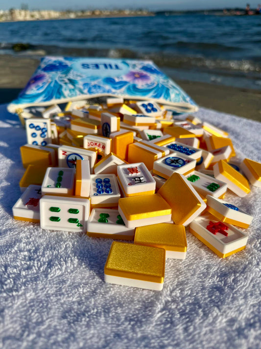 Mahjong tiles on a sandy surface with a bag labeled 'TILES' in the background.
