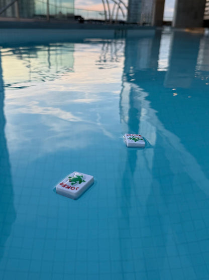 Two floating mahjong tiles on a pool surface with reflections.
