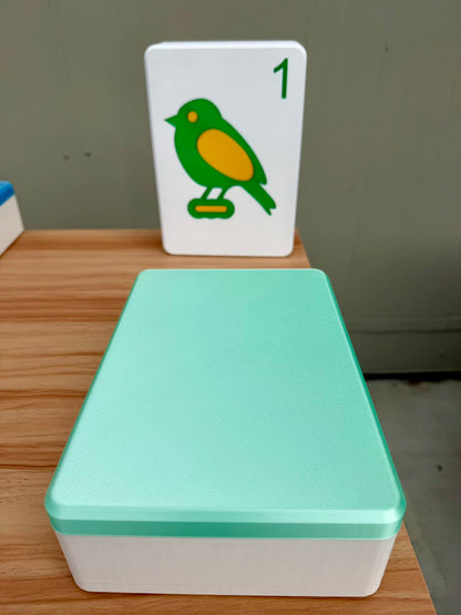 Light green Mahjong container with a card featuring a bird design on a wooden surface.