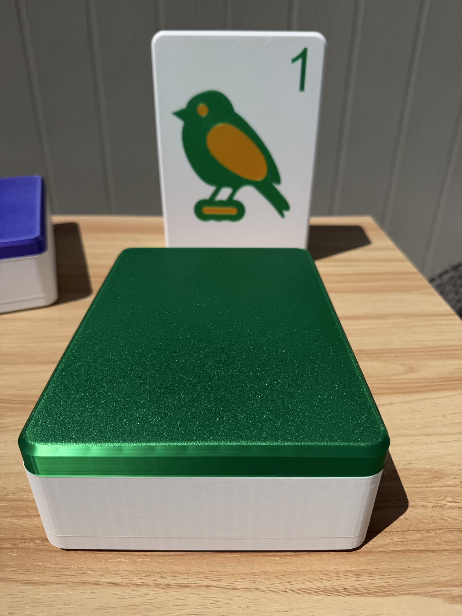 Green and white box with a card featuring a bird illustration on top, on a wooden surface.