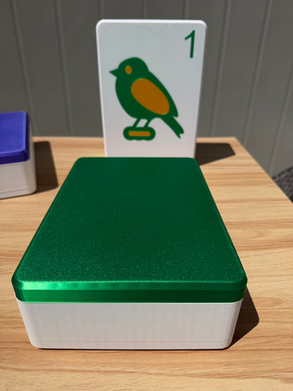 Green and white box with a card featuring a bird illustration on top, on a wooden surface.