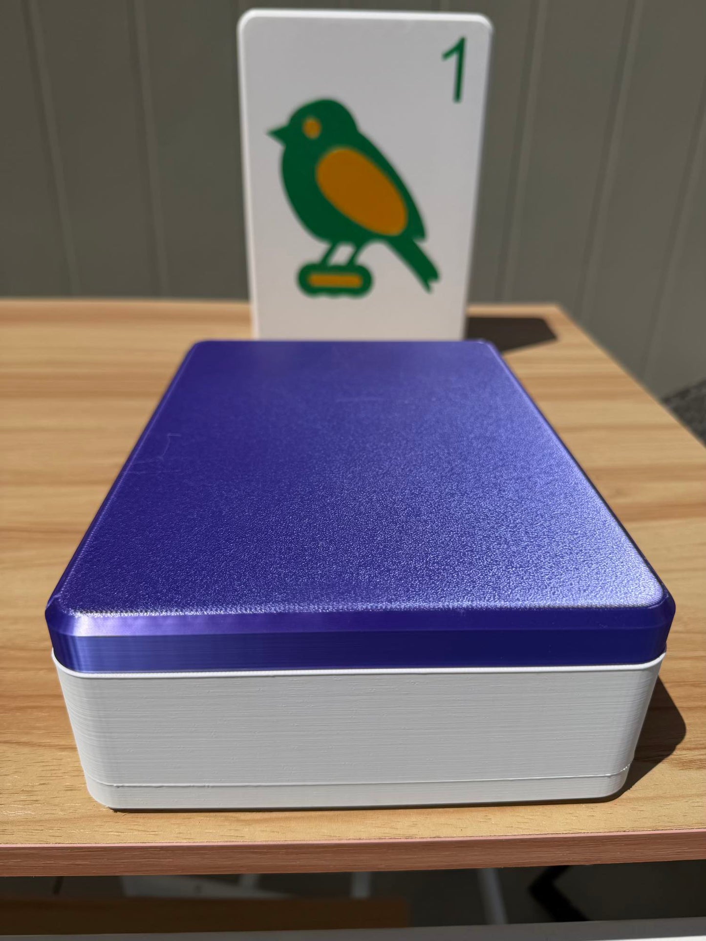 Silk Purple and white box with a card featuring a bird illustration on a wooden surface.