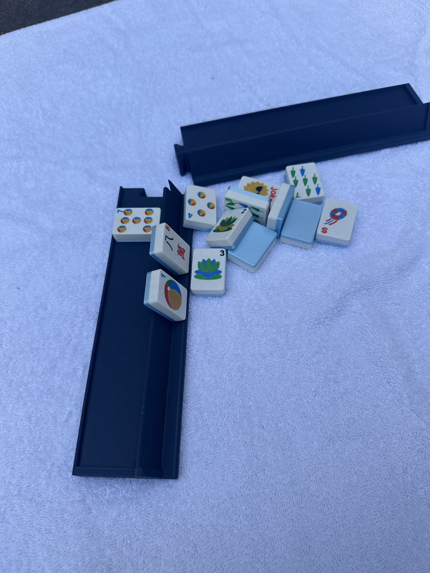 Set of American Mahjong Tiles Sitting Next to An American Mahjong Travel Rack That is Perfect for travel because it can split it two and fit in a small bag but also handle large tiles.