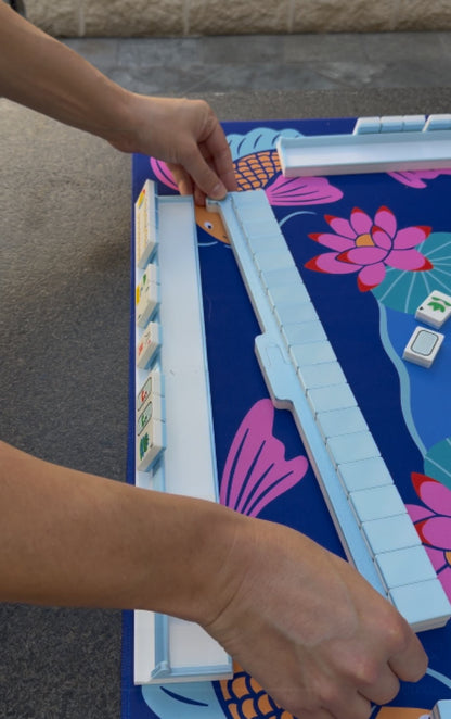 Hands assembling Spools pool mahjong racks on a poolside playing mat.
