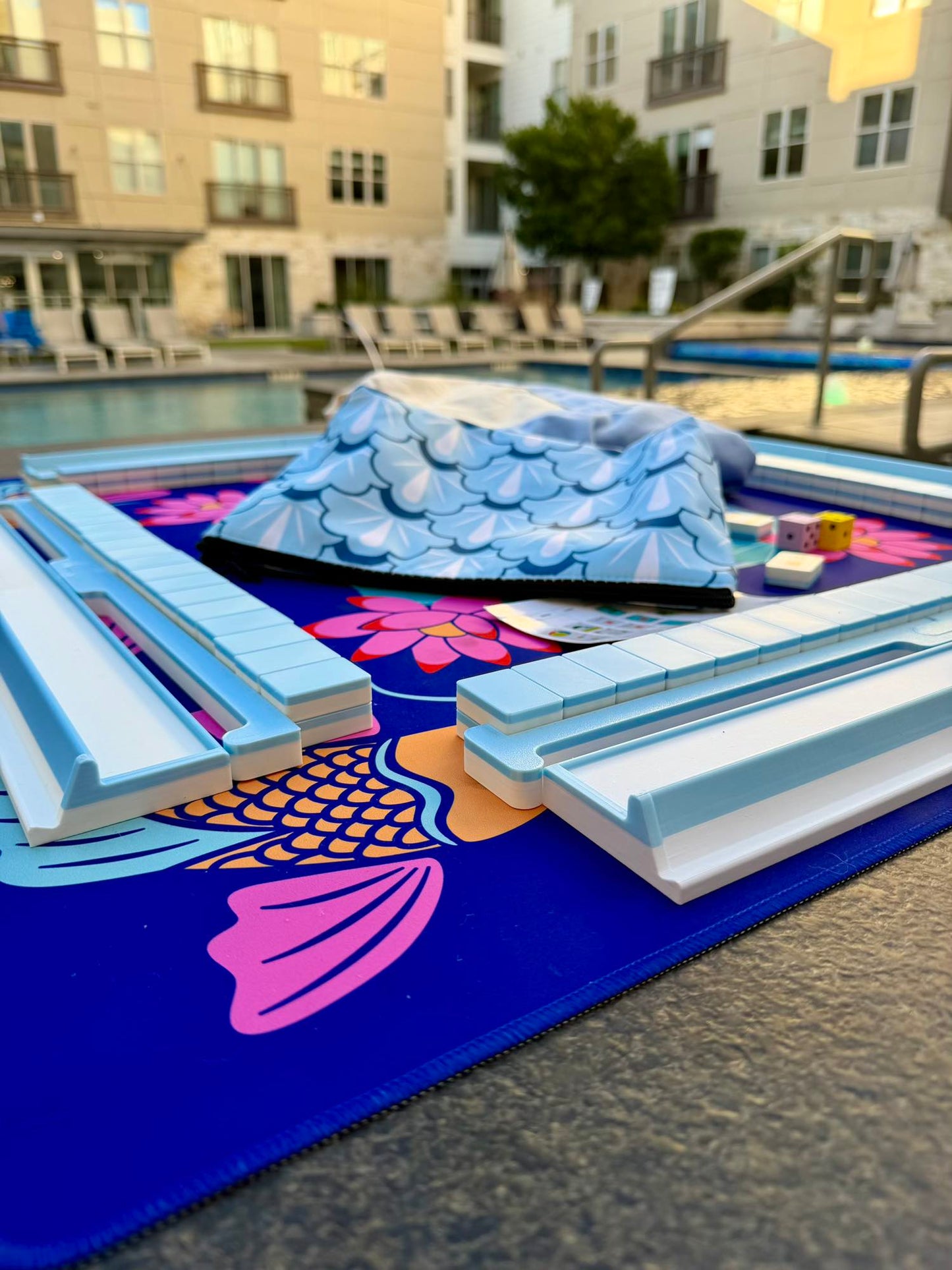 Spools pool mahjong set with floating tiles and racks arranged on a poolside playing mat, designed for water and outdoor play.