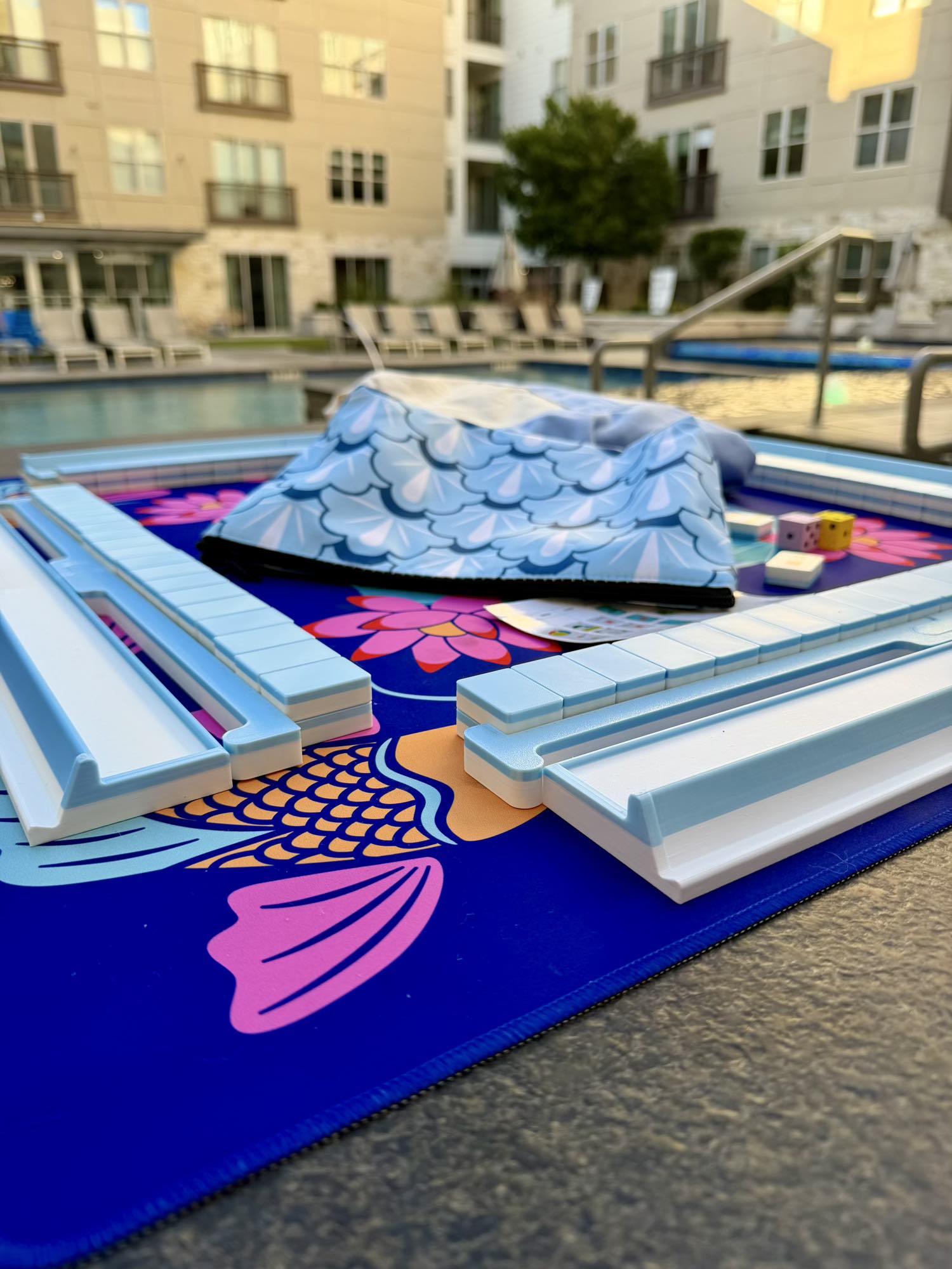 Spools pool mahjong set with floating tiles and racks arranged on a poolside playing mat, designed for water and outdoor play.