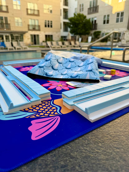 Spools pool mahjong set with floating tiles and racks arranged on a poolside playing mat, designed for water and outdoor play.