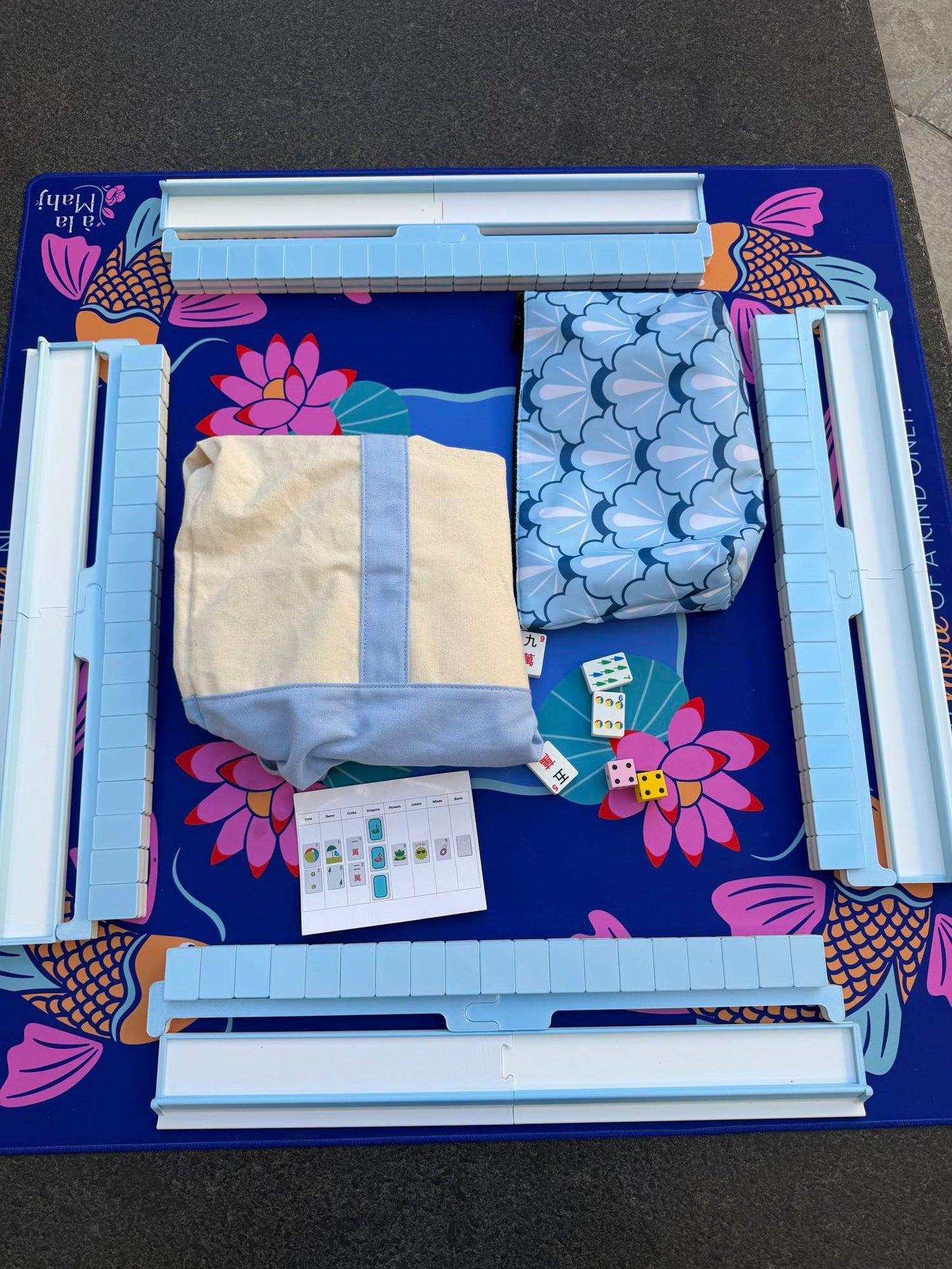 Spools pool mahjong set laid out with floating tiles, racks, accessories, and carrying bag on a poolside mat.