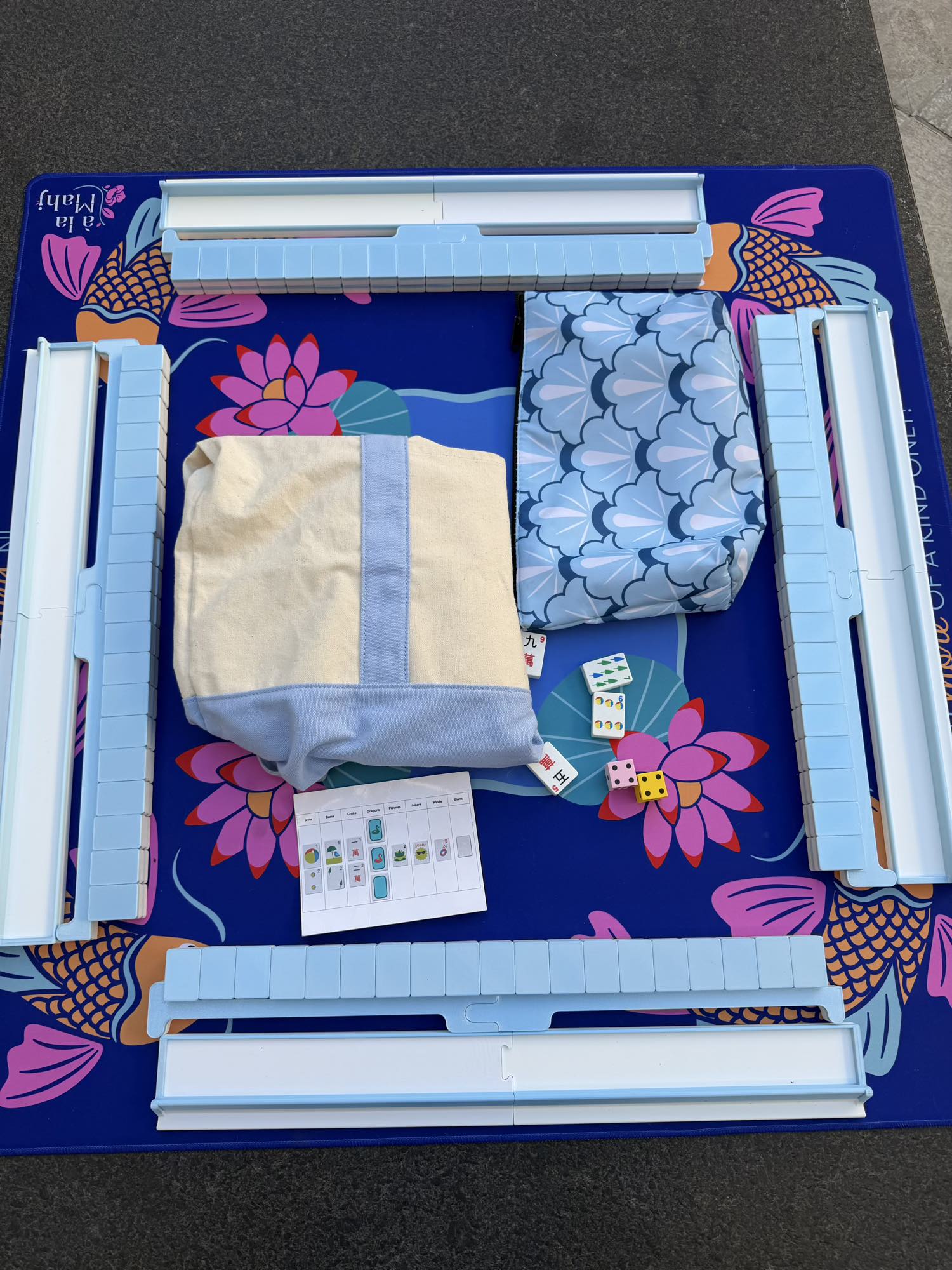 Spools pool mahjong set laid out with floating tiles, racks, accessories, and carrying bag on a poolside mat.