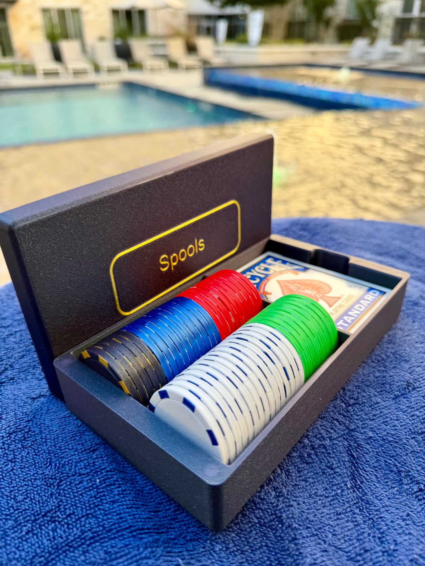 Spools travel poker set opened beside a pool, showing lightweight poker chips and playing cards ready for play.