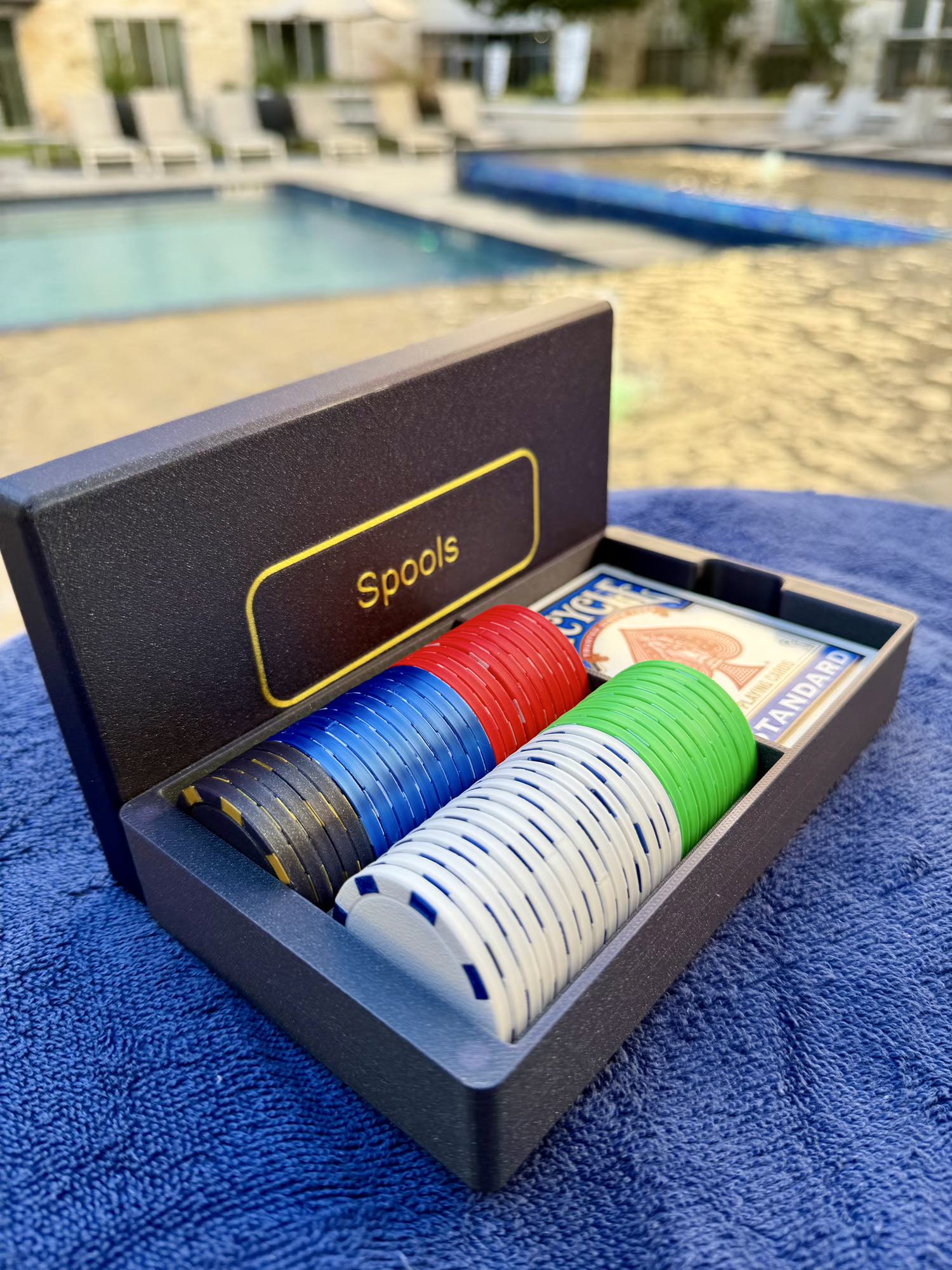 Spools travel poker set opened beside a pool, showing lightweight poker chips and playing cards ready for play.