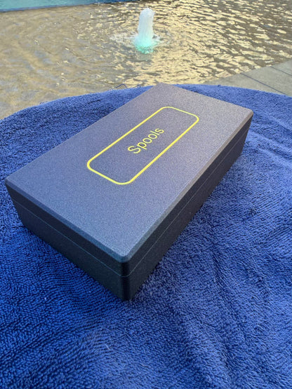 Spools travel poker set closed in a slim gray case with logo, shown poolside on a blue towel.
