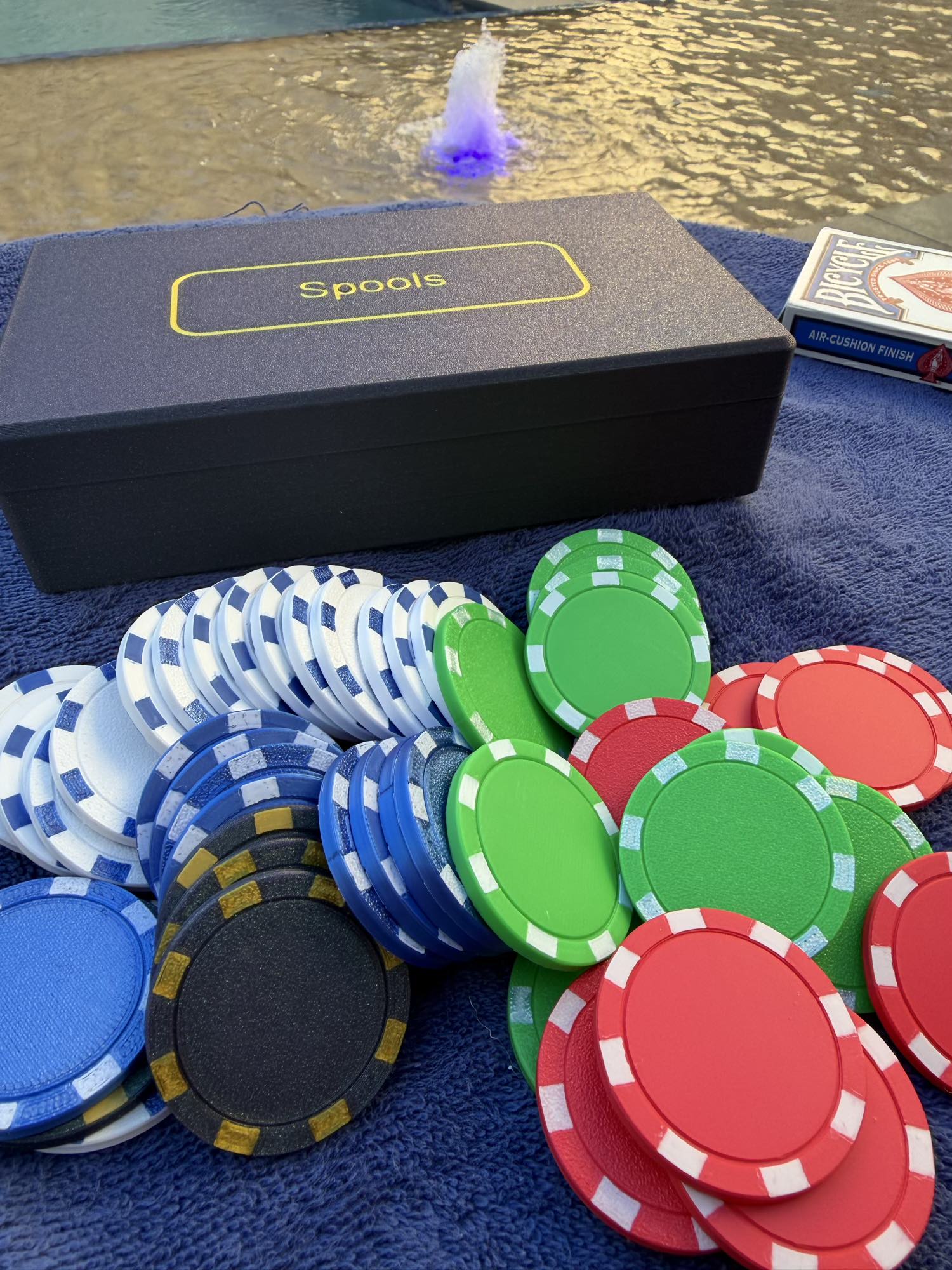 Spools travel poker set with lightweight poker chips spread out next to the case and a deck of cards by a pool.