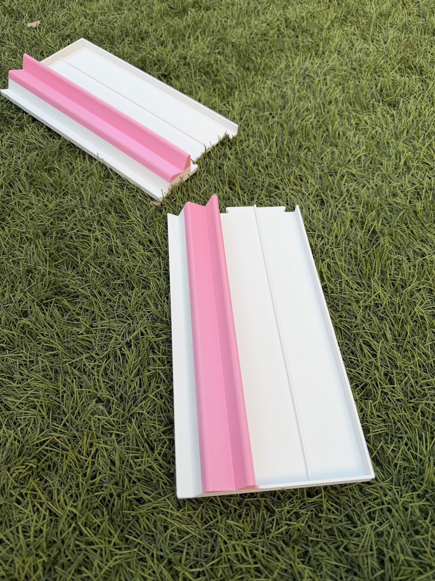 Two white portable Two Player Mahjong racks with pink rails, shown side-by-side on a grass surface.
