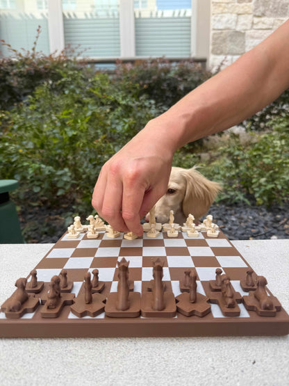 Hand moving a cream dachshund chess piece on the Wienerdog Chess set, with a dachshund dog watching in the background