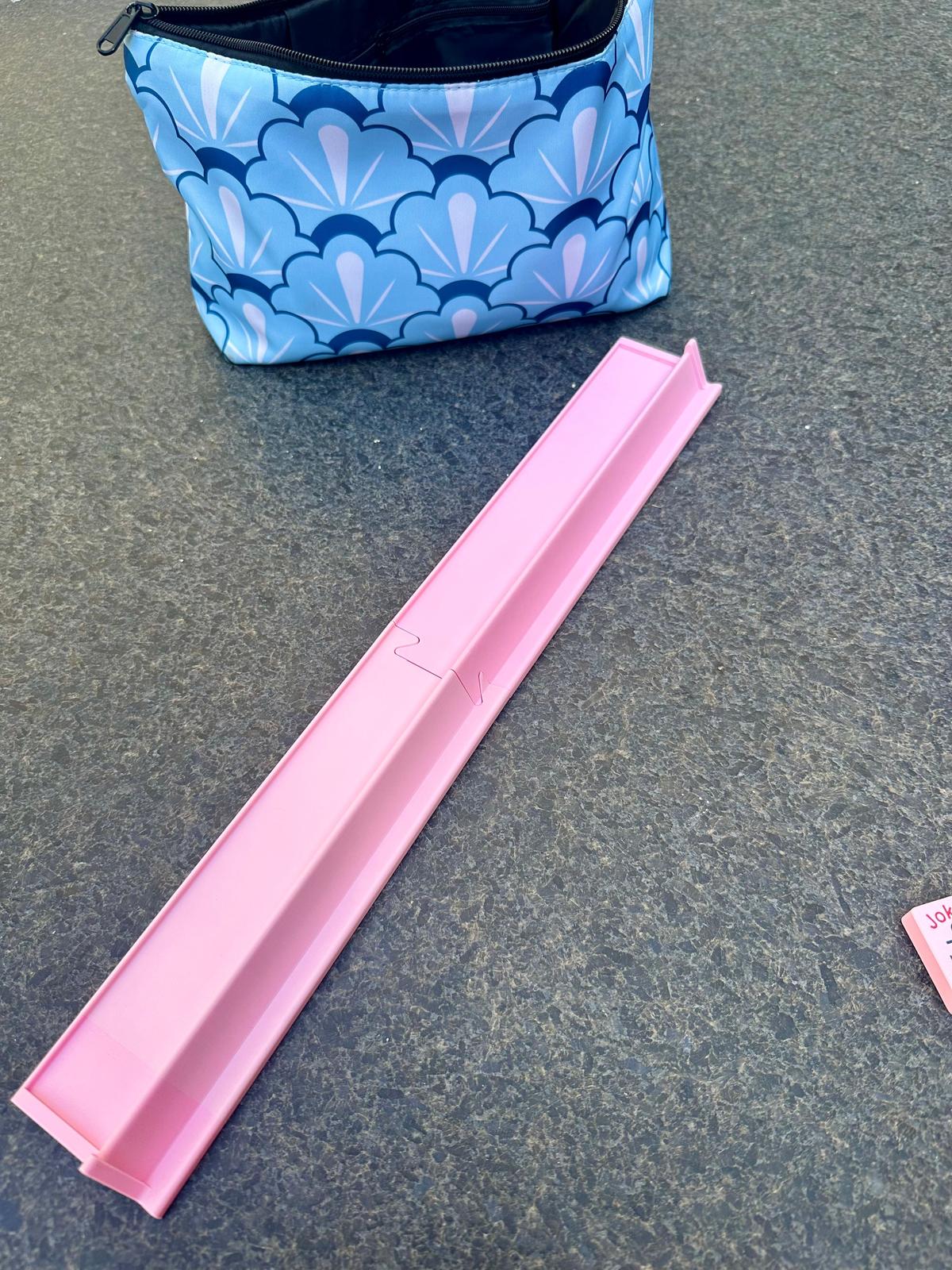 Empty pink floating mahjong rack displayed on outdoor table with a blue scallop-patterned carrying bag in the background