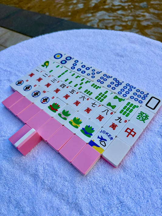 Pink full-size Mahjong tiles arranged on a travel rack from the Spools Travel Mahjong Bundle, including cracks, bams, dots, winds, and jokers.