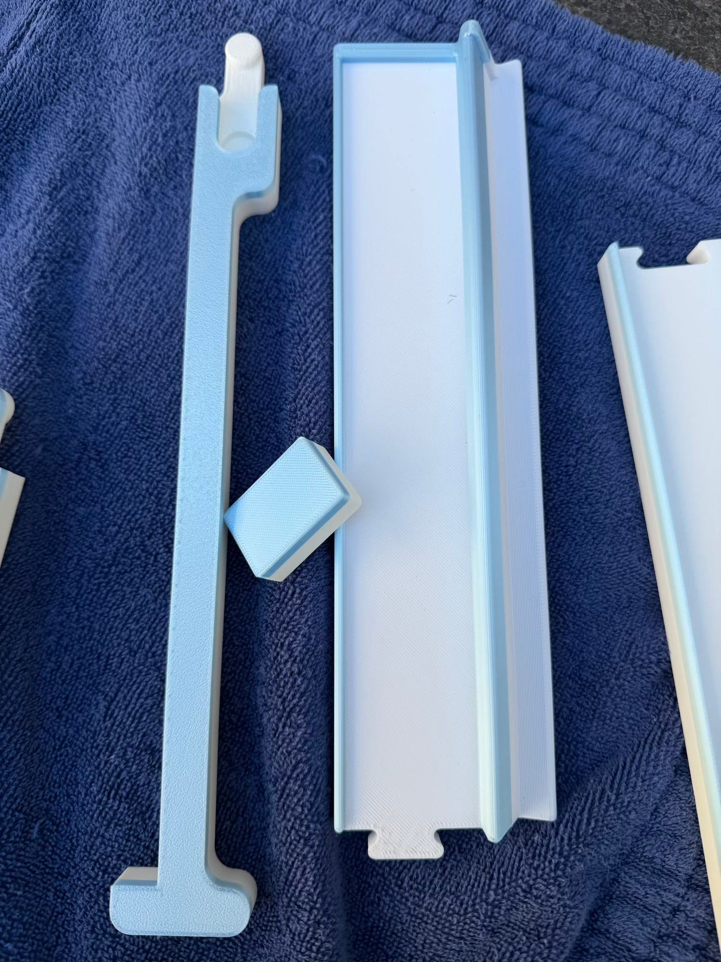 Overhead view of the blue Travel Mahjong rack and pusher components laid out on a navy towel.