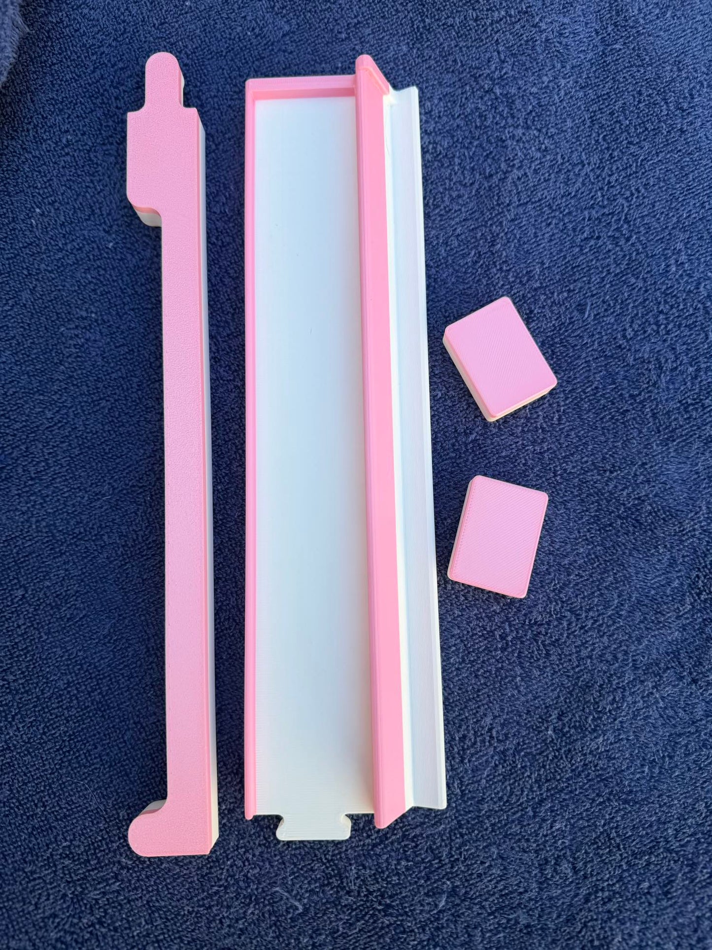 Overhead image of the pink Travel Mahjong rack pieces and tiles displayed on a navy towel.