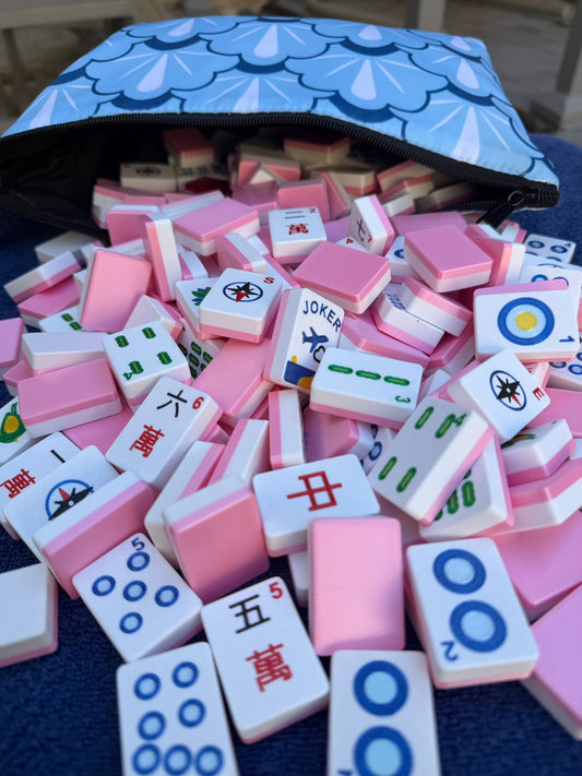 Close-up of pink Compass Travel Mahjong tiles spilling from a blue patterned travel case, showcasing lightweight full-size American Mahjong tiles.